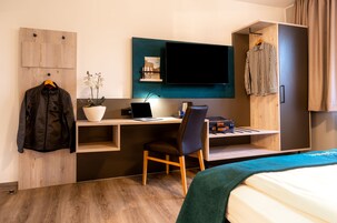 Una habitación de hotel moderna con un escritorio de madera, una computadora portátil, una silla, una cama, un televisor y un armario.
