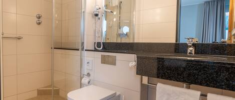 A modern bathroom with a glass shower enclosure, a white toilet, a vanity with a black countertop, and a large mirror.