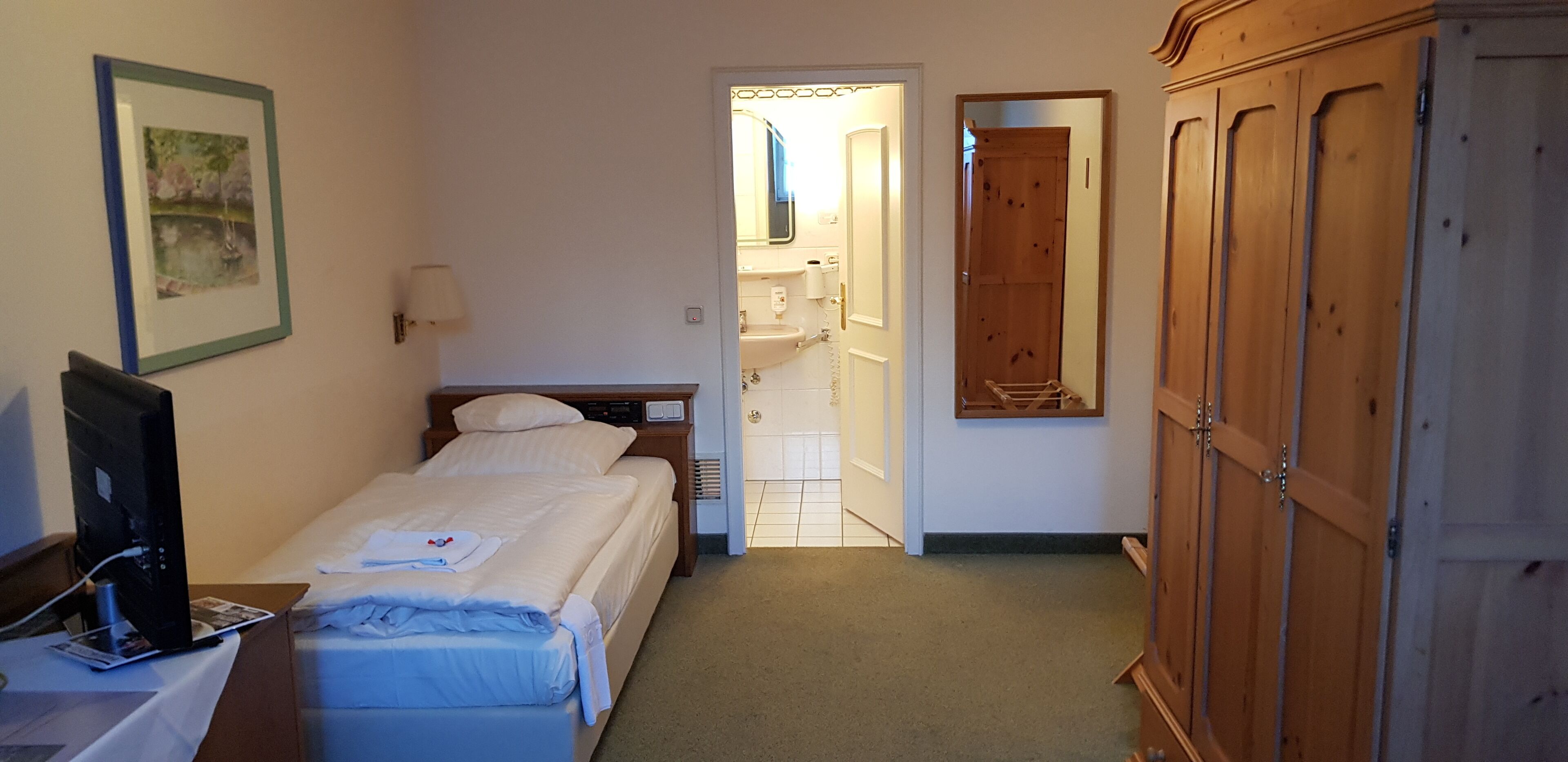 Une chambre d’hôtel avec un lit, un bureau équipé d’un ordinateur, une armoire et une salle de bain visible à travers une porte ouverte.