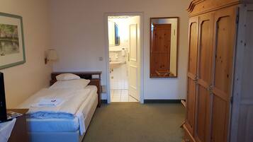 Une chambre d’hôtel avec un lit, un bureau équipé d’un ordinateur, une armoire et une salle de bain visible à travers une porte ouverte.