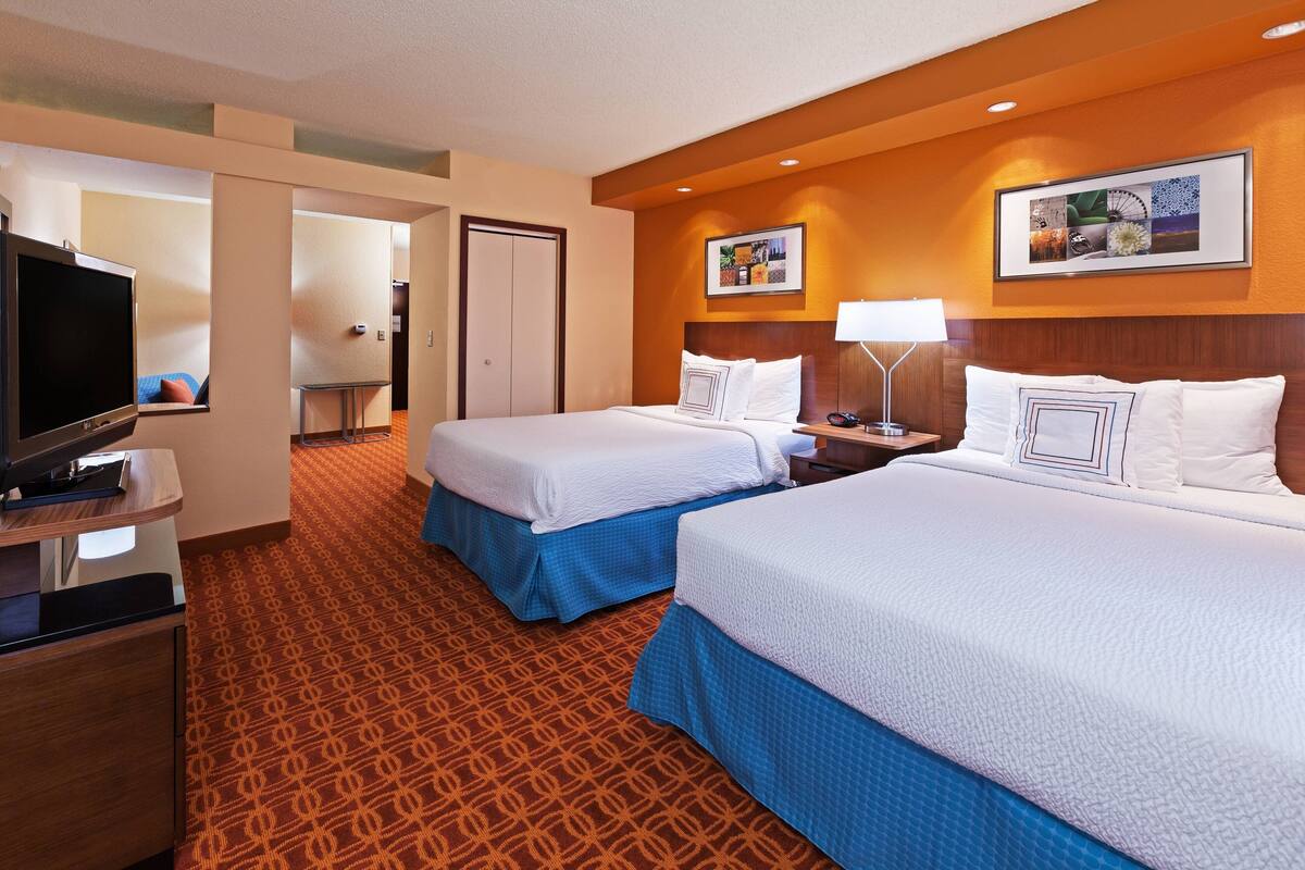A hotel room with two beds, a TV, a desk, and a patterned carpet.
