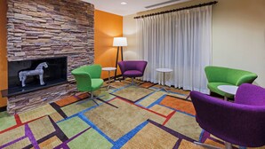 A room with a stone fireplace, colorful carpet, green and purple chairs, and a white table. - Fairfield Inn and Suites by Marriott Austin Northwest/Domain (Austin)