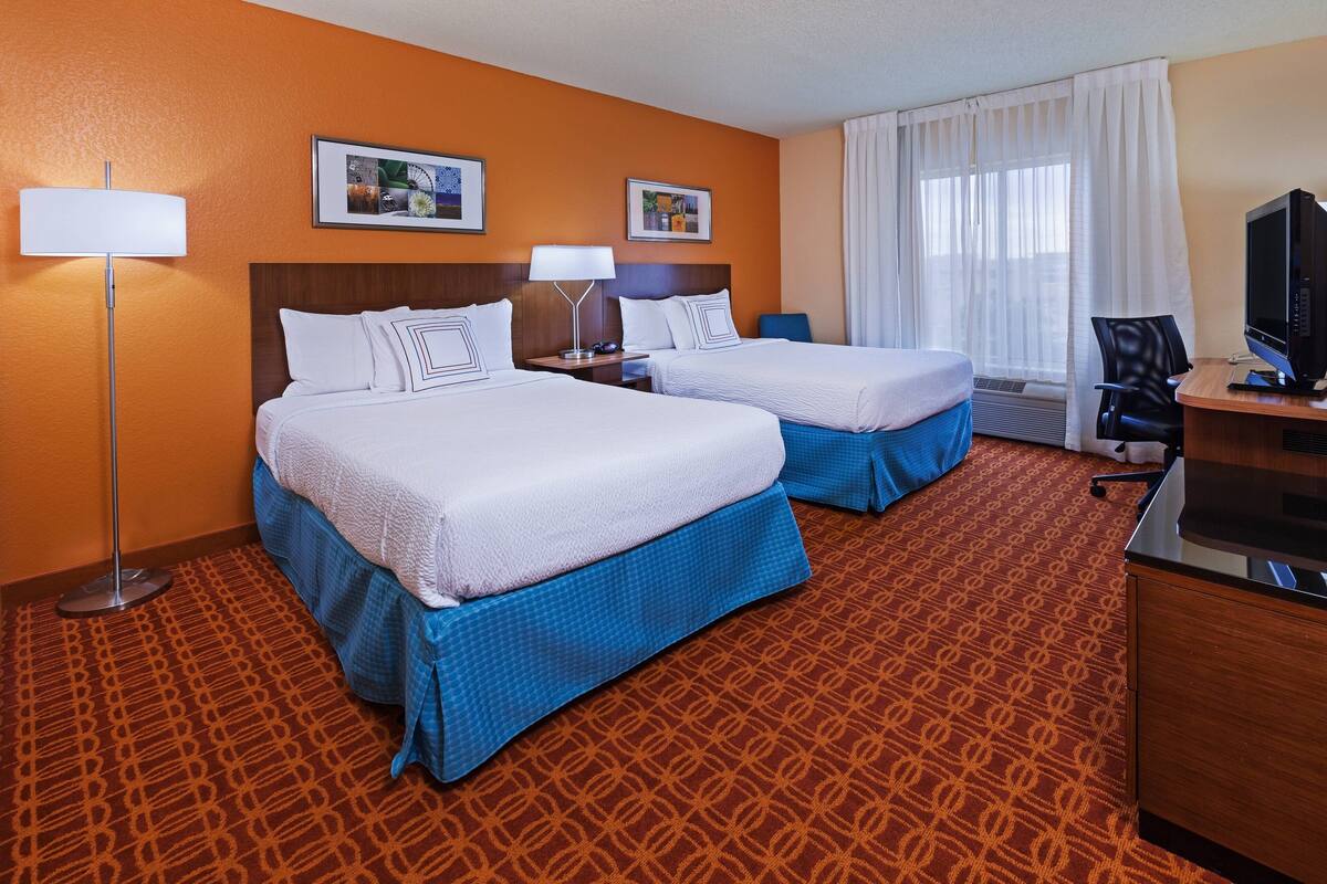 A hotel room with two beds, a desk with a computer, a TV, and two lamps.