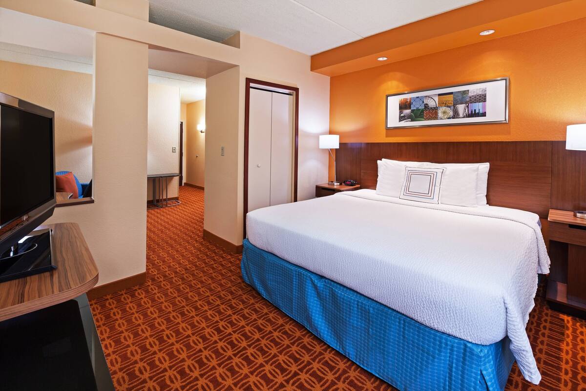 A hotel room with a large bed, a television, a desk, and a framed picture on the wall.