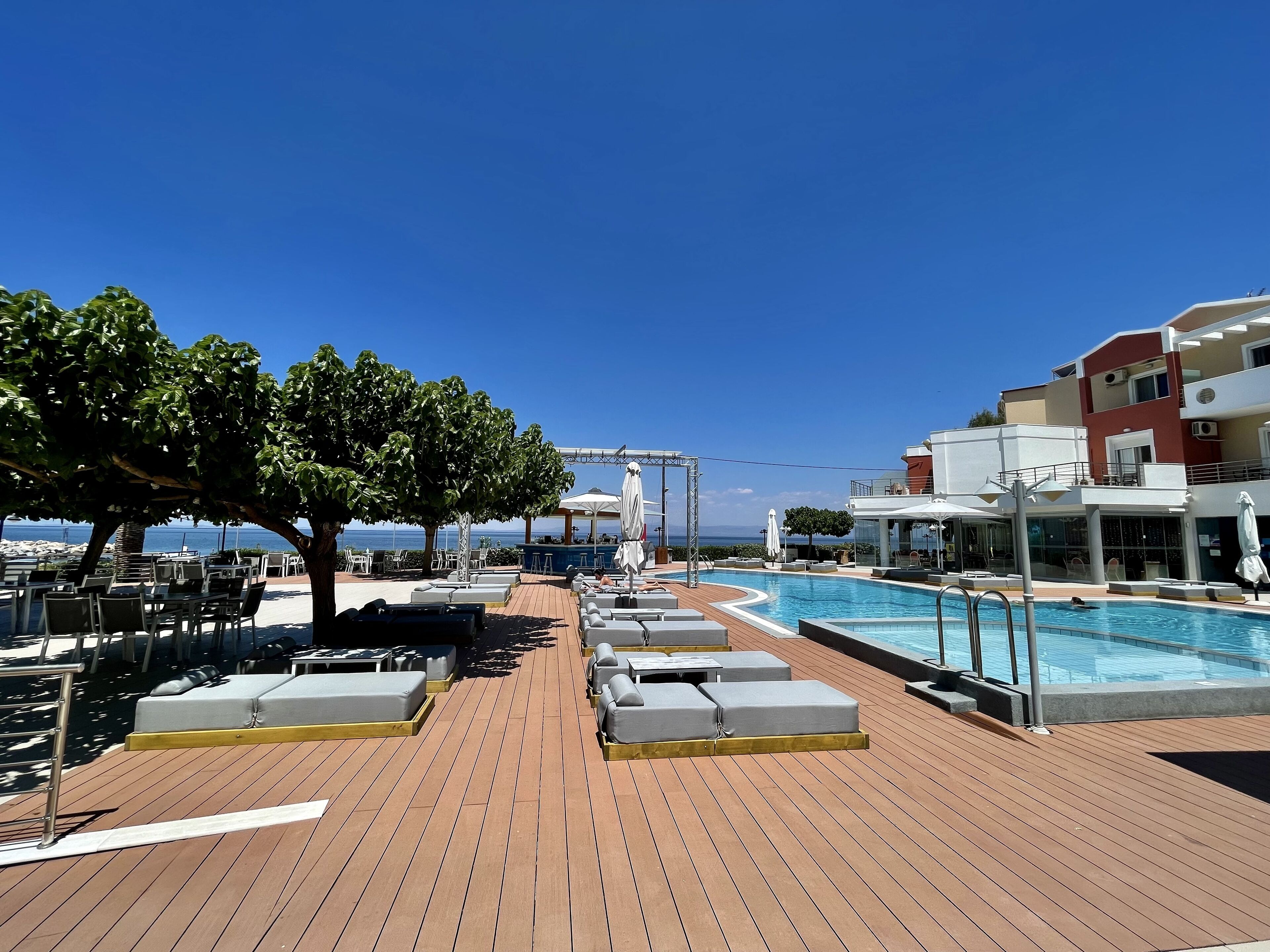 A poolside area with lounge chairs and a pool, overlooking the sea.