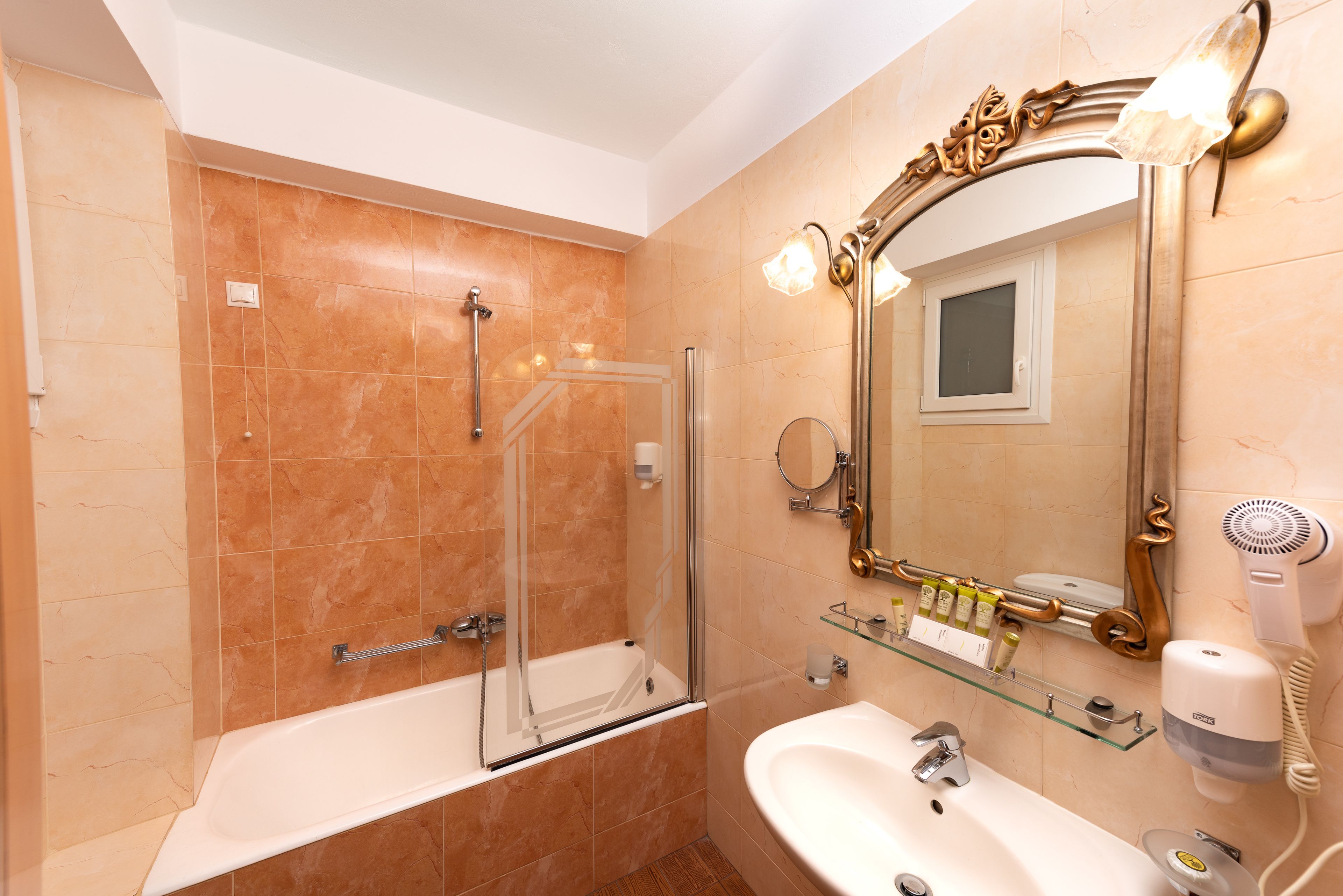 A bathroom with a glass-enclosed shower, a sink, a mirror, and a hairdryer on the wall.