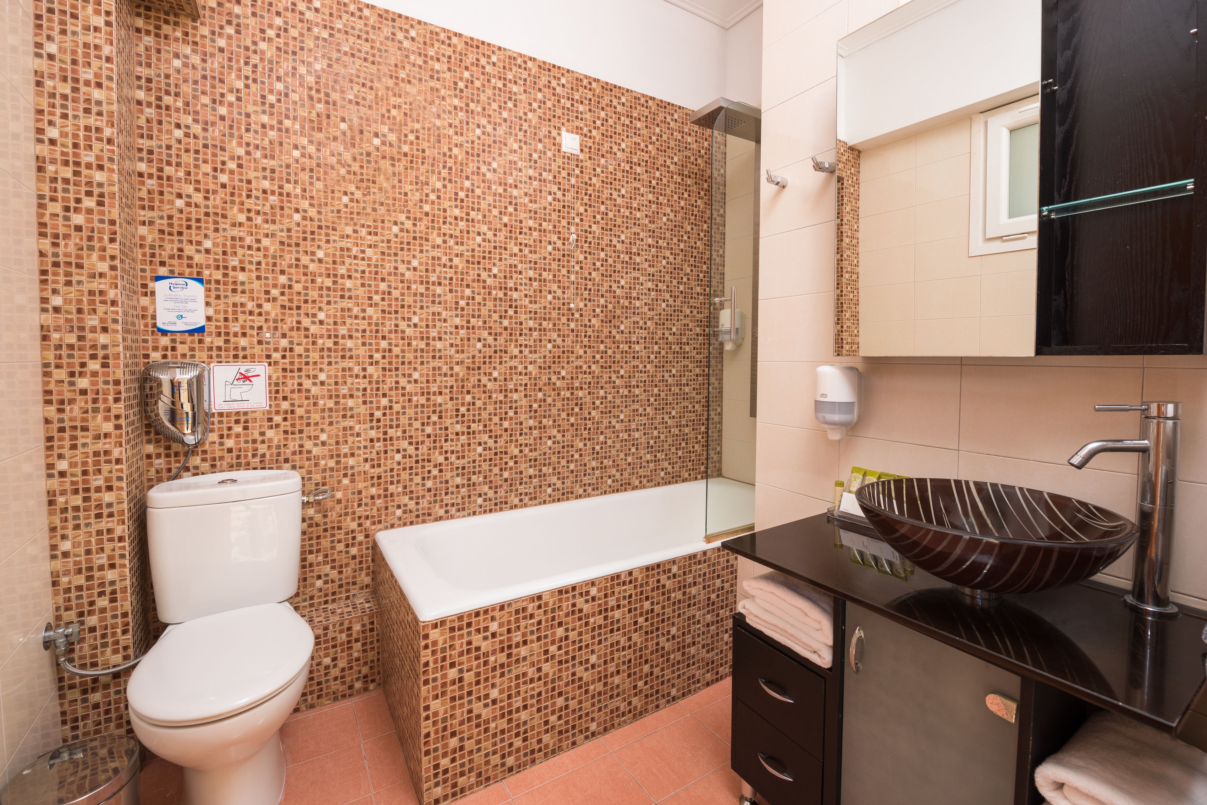 Un bagno con parete in mosaico, un WC bianco, una vasca da bagno, un lavandino scuro con lavabo a incasso e uno specchio sopra il lavandino.