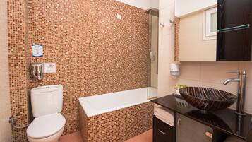 Un bagno con parete in mosaico, un WC bianco, una vasca da bagno, un lavandino scuro con lavabo a incasso e uno specchio sopra il lavandino.