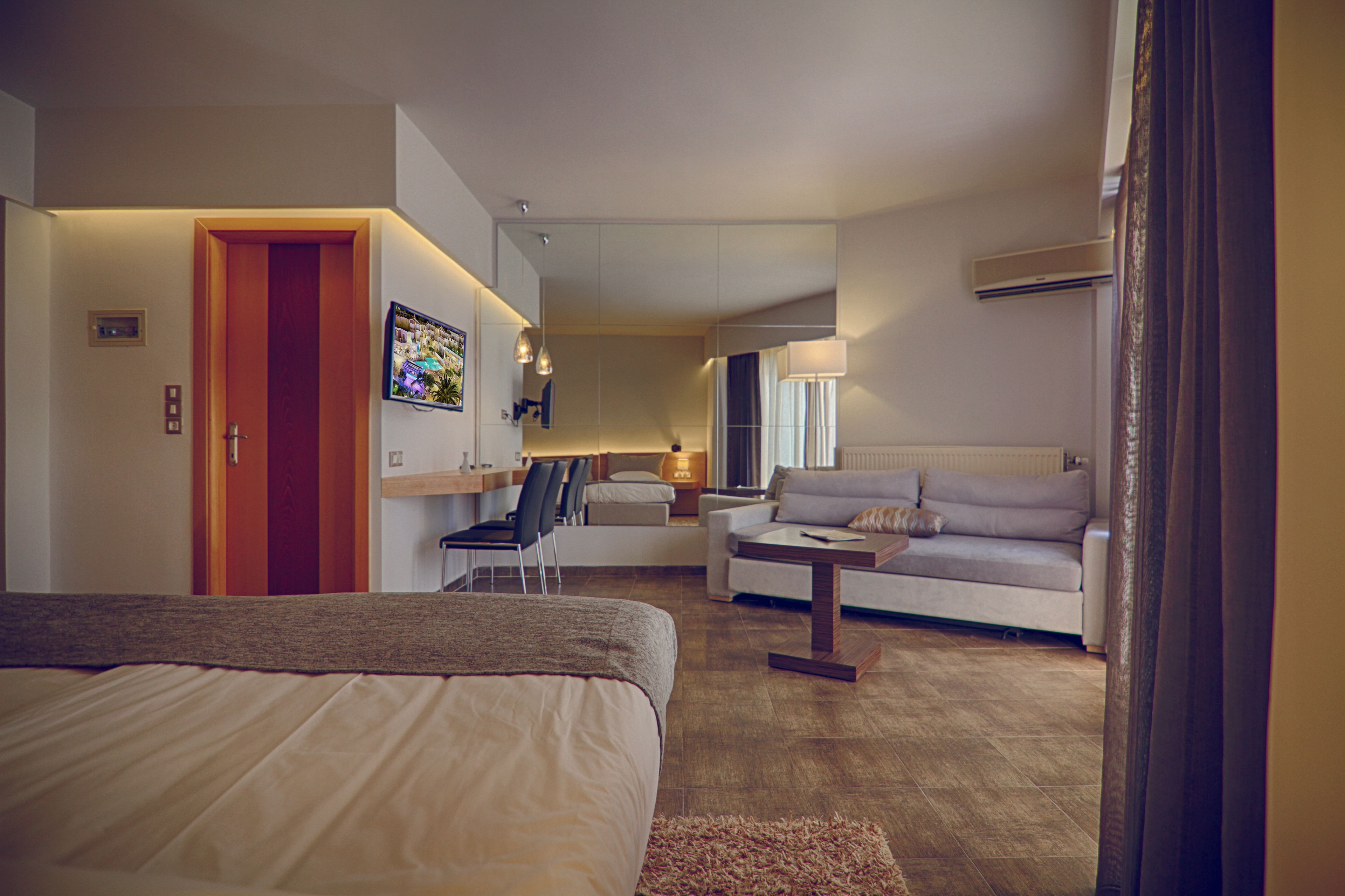 A modern hotel room with a bed, a sofa, a desk, and a TV.