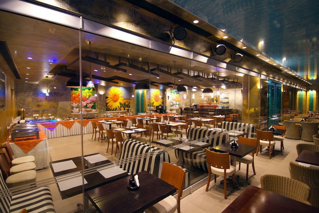 Un restaurante con una decoración moderna, que presenta cabinas y mesas a rayas, una zona de bar y un mural con girasoles.