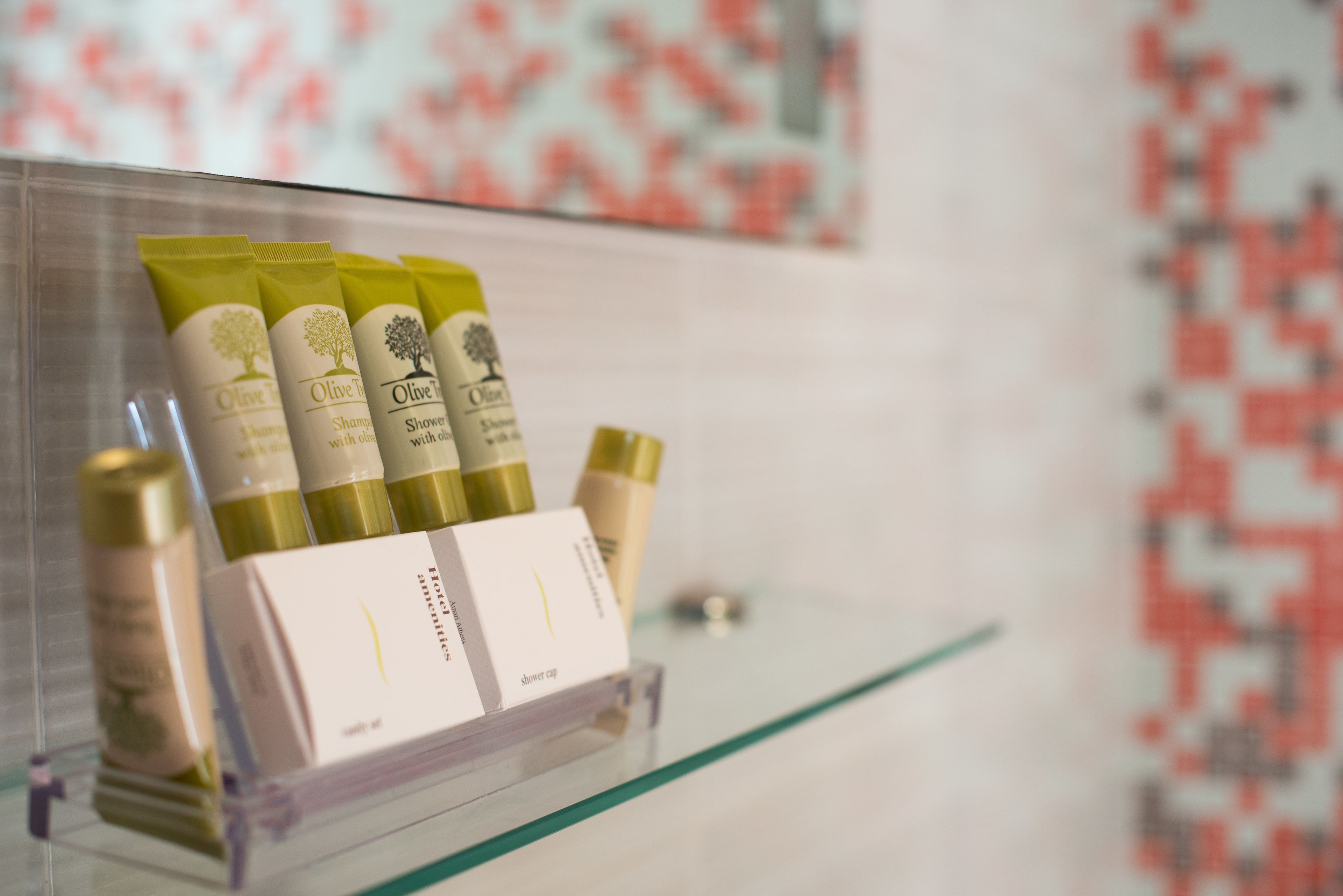A display of olive oil products on a clear shelf in a bathroom.