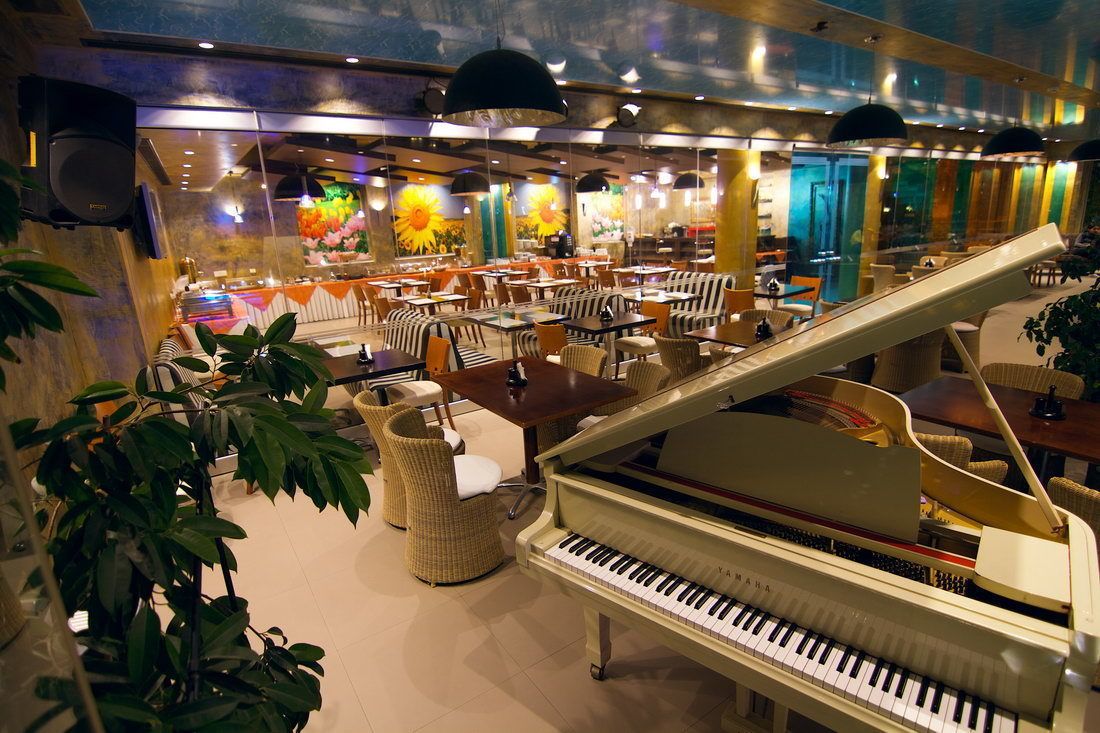 A spacious indoor dining area with a grand piano, comfortable seating, and a vibrant mural in the background.