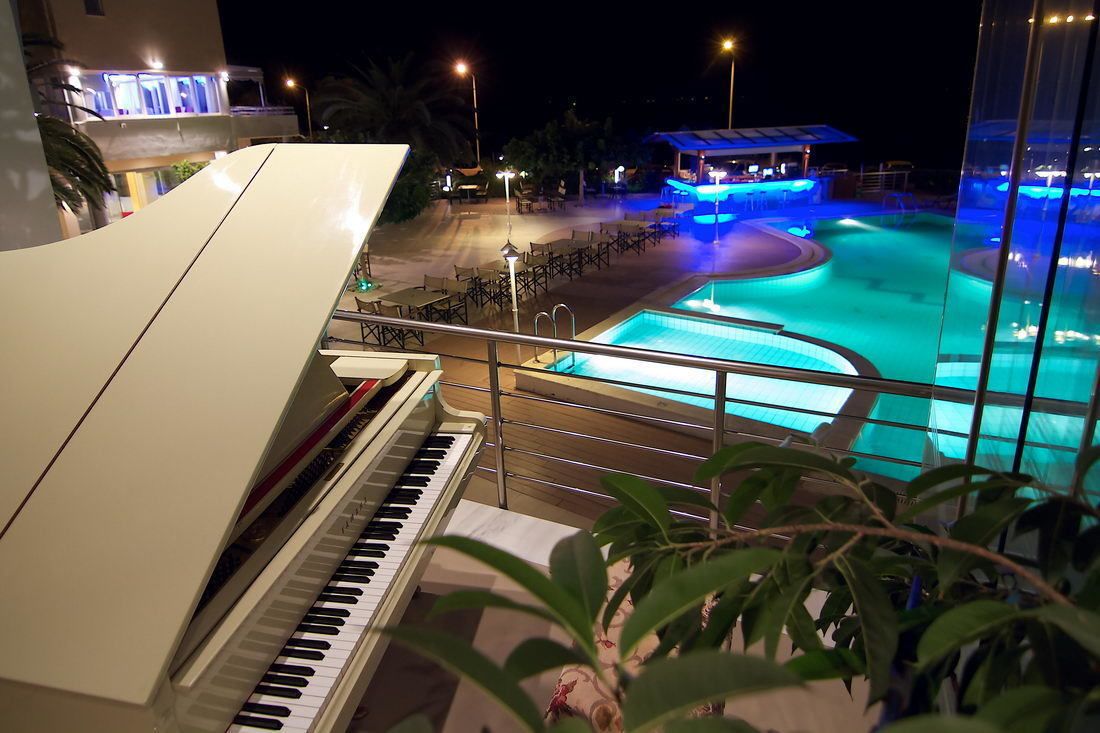 A piano overlooking a pool area with a covered seating area and a building in the background.