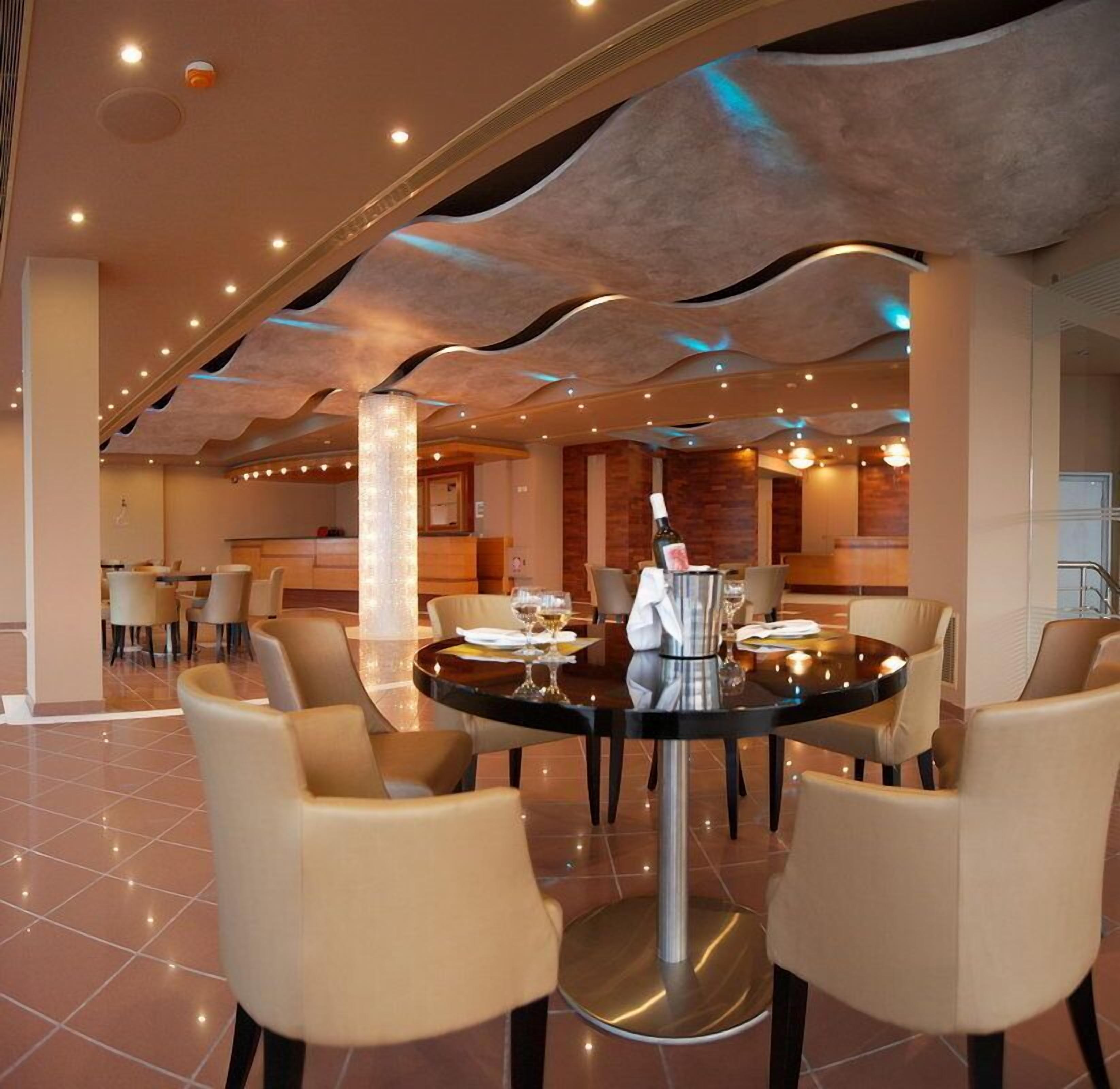 A modern dining area with round tables and beige chairs, featuring a central column and ambient lighting.