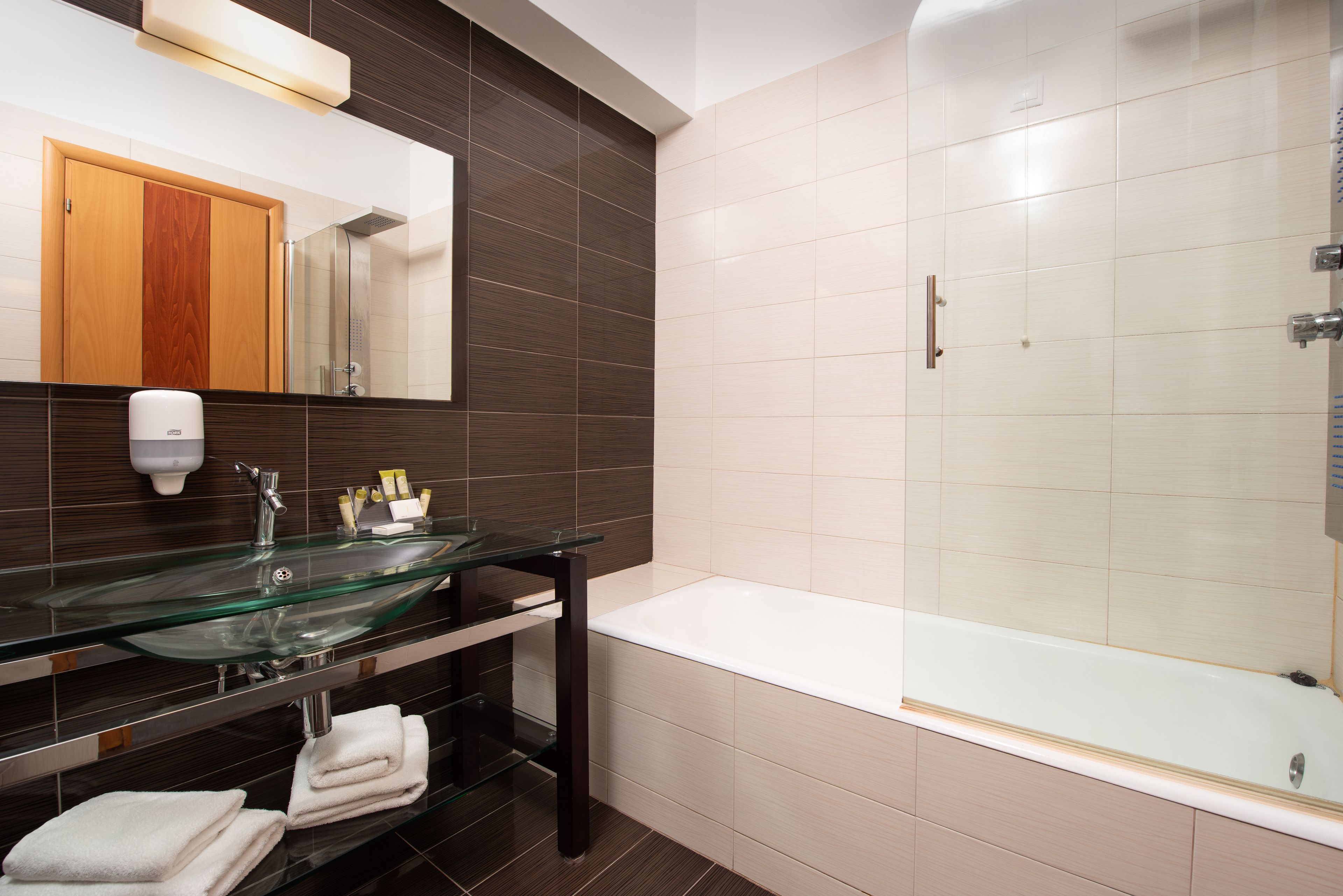 Un bagno moderno con lavabo in vetro, uno specchio grande, una vasca da bagno bianca e uno spazio doccia.