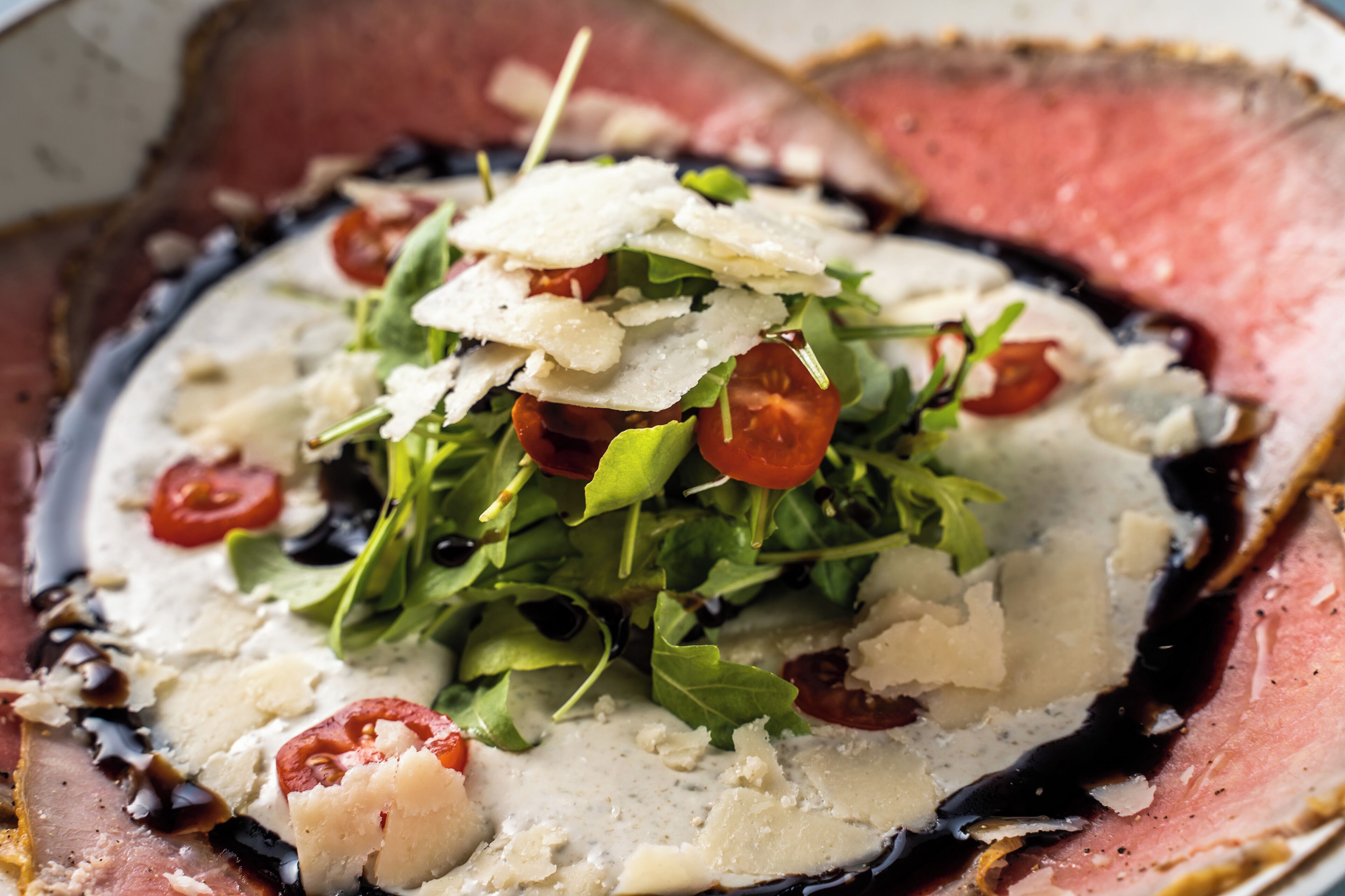A plate of food with arugula, cherry tomatoes, shaved cheese, and a creamy sauce.