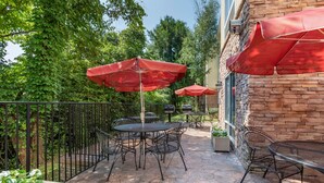 An outdoor patio with stone flooring, metal tables and chairs, and red umbrellas. - Fairfield Inn Suites by Marriott Cherokee (Cherokee)