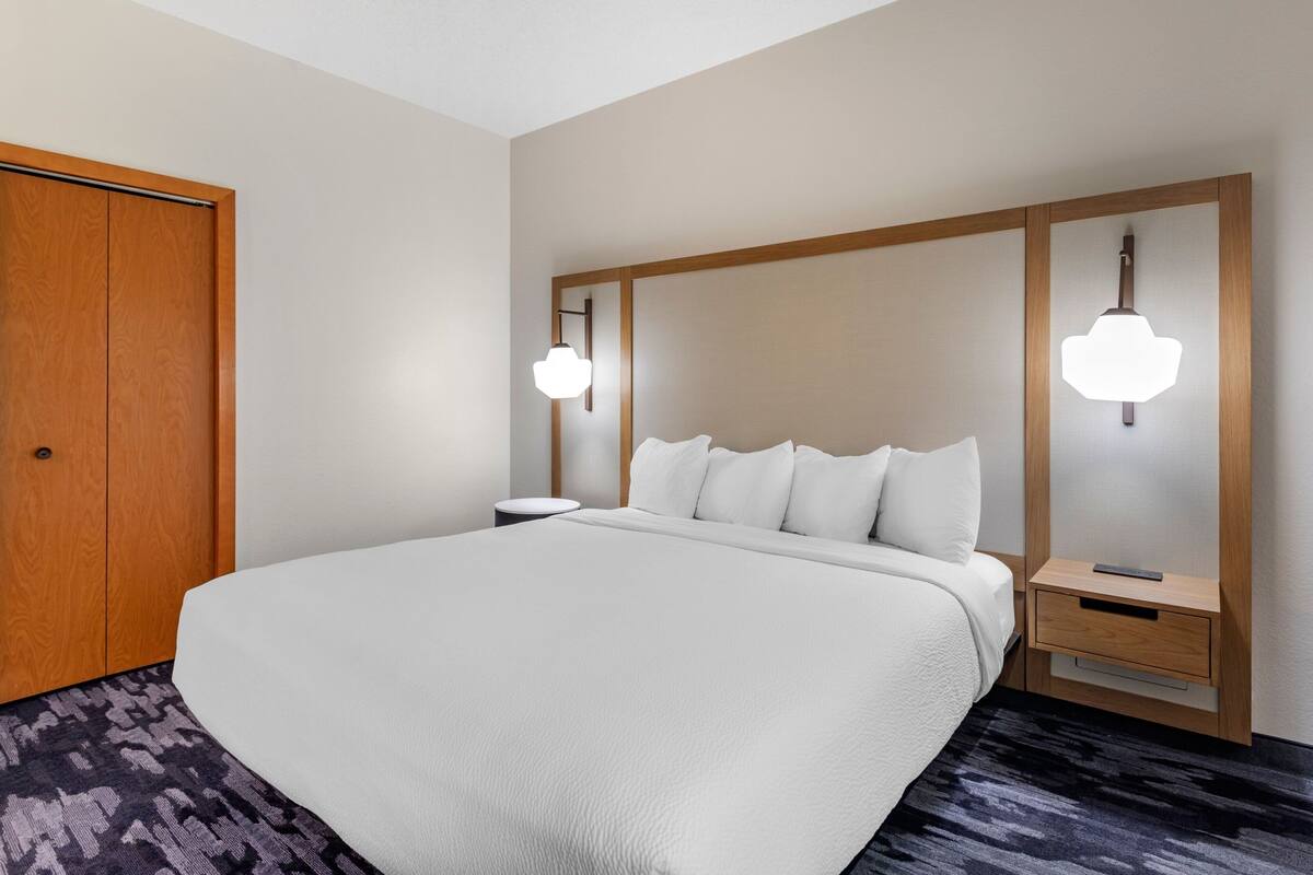 Une chambre d’hôtel avec un grand lit, une tête de lit en bois, des tables de chevet et une armoire.
