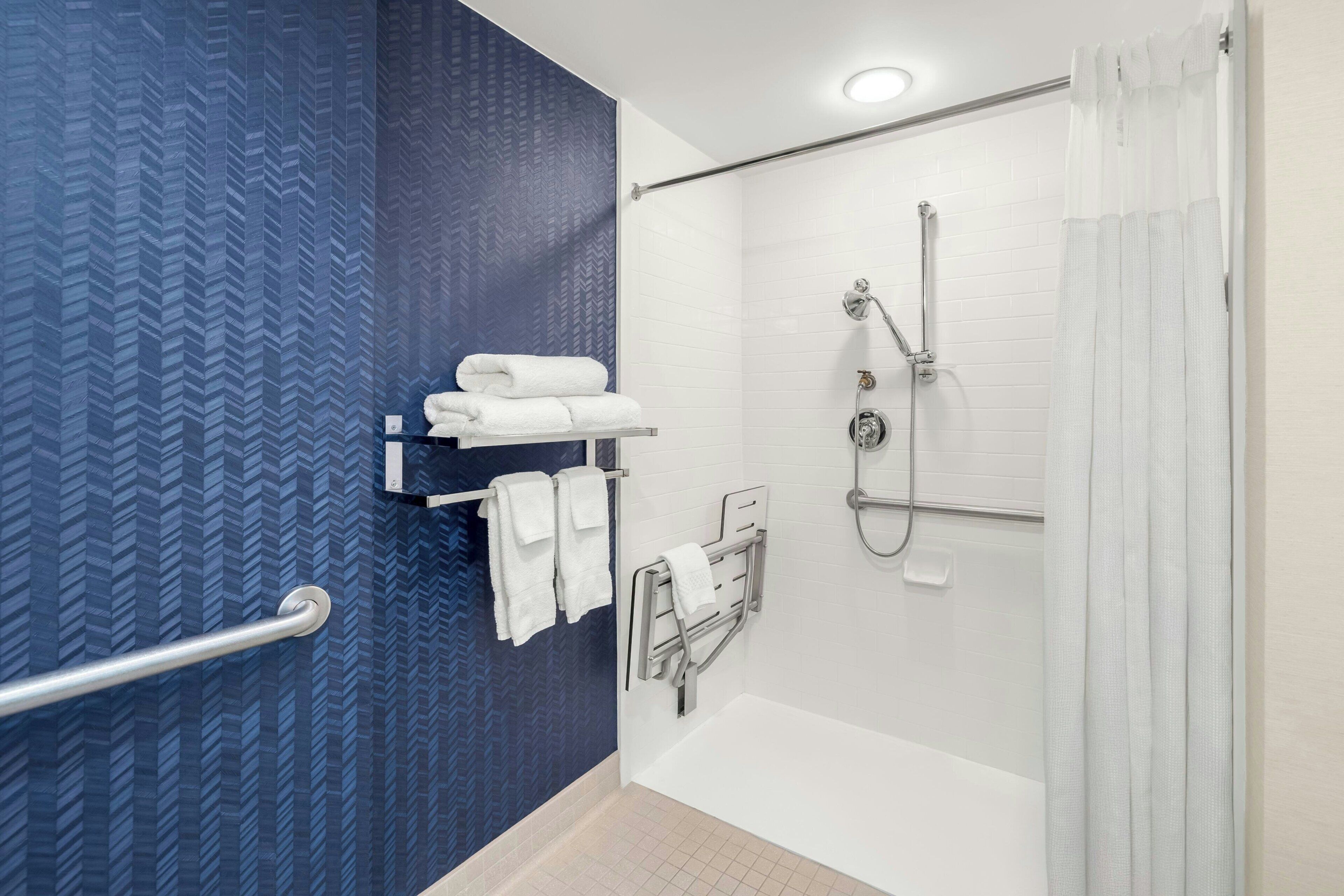 A modern bathroom with a blue patterned wall, a white bathtub, a shower with a handheld showerhead, and a grab bar.