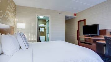 Habitación de hotel con una cama grande, televisión, escritorio y baño visible a través de una puerta abierta.