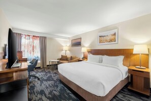 A hotel room with a large bed, a desk with a computer, a chair, a small table, and two lamps. - Fairfield Inn by Marriott Burlington Williston (Williston)