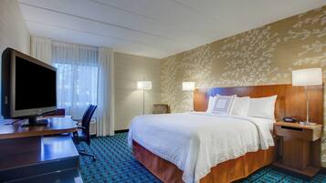 Una habitación de hotel con cama, escritorio con televisor, dos lámparas de noche y alfombra estampada.