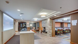 Eine Hotellobby mit einer Rezeption, einem Kamin aus Stein und einem Essbereich mit Stühlen und Tischen.