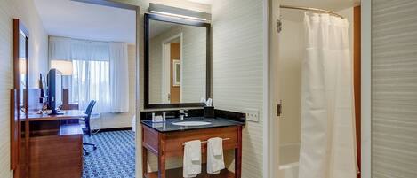 A hotel bathroom with a wooden vanity, a large mirror, a shower with a white curtain, and a patterned floor.