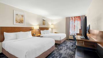 A hotel room with two beds, a desk with a computer, a TV, and artwork on the walls.