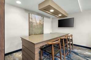 Un salón de conferencias con una larga mesa, cuatro sillas, un televisor montado y una lámpara en el techo.