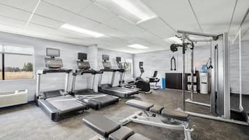 Un gimnasio con cintas de correr, máquinas de pesas y un espejo grande.