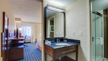Un baño de hotel con un espejo grande, un lavamanos, una ducha y un escritorio con una silla.