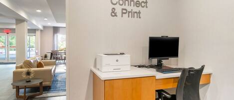 Ein Hotel-Rezeptionsbereich mit einem Schreibtisch, Drucker und Computer. An der Wand befindet sich ein Schild mit der Aufschrift 'Connect & Print'.