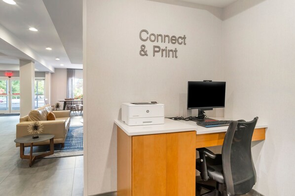 A hotel reception area with a desk, printer, and computer. There is a sign that reads "Connect & Print" on the wall.