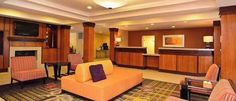 Um saguão de hotel com um sofá, cadeiras listradas, uma recepção e uma televisão fixada na parede.