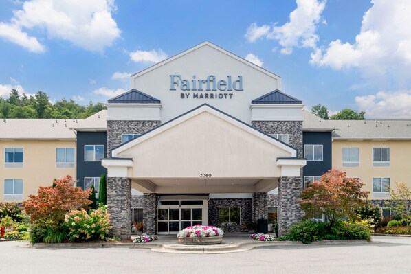 Entrada de um hotel Fairfield by Marriott, com fachada de pedra, portas de entrada amplas e área ajardinada com flores.