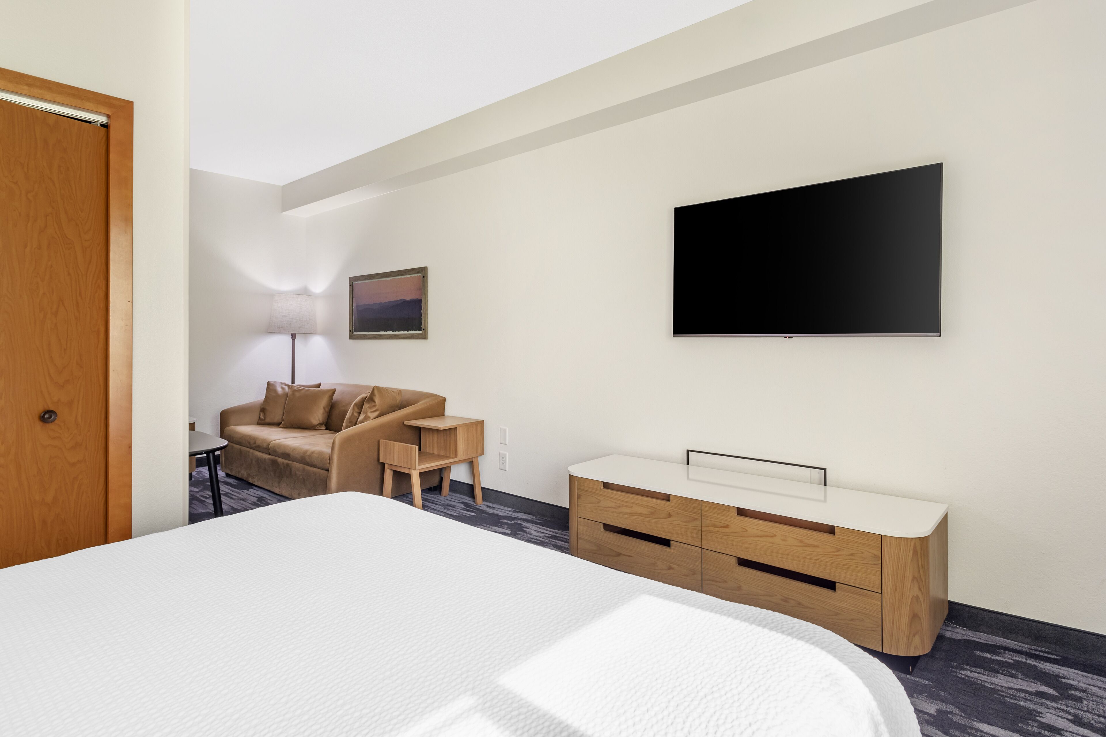 Ein Hotelzimmer mit Bett, einer Couch, einem Fernseher, einem Schreibtisch und einer Lampe.
