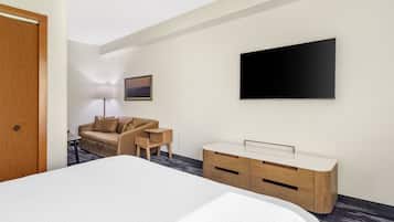 A hotel room with a bed, a sofa, a TV, a desk, and a lamp.