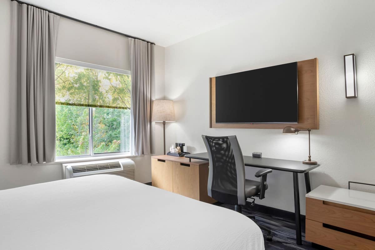 A hotel room with a bed, a desk, a chair, a TV, and a window with curtains.