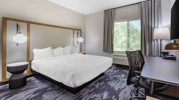 A hotel room with a large bed, a desk with a chair, a lamp, and a window with curtains.
