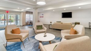 Eine moderne Lobby mit Sitzgelegenheit, einem Wand-Fernseher und einem großen Fenster mit Ausblick ins Freie.
