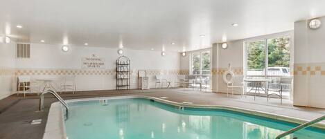 An indoor swimming pool with clear water, surrounded by white chairs and tables, and a sign indicating no diving or lifeguard on duty.