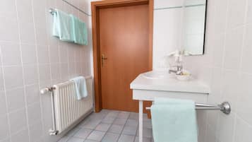 Um banheiro com porta de madeira, paredes com azulejos brancos, pia branca e porta-toalhas.