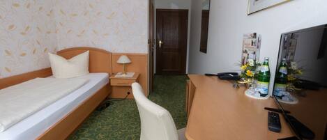 Une chambre d’hôtel avec un lit, un bureau équipé d’un ordinateur, une chaise, une lampe et une petite table avec des boissons et une télécommande.
