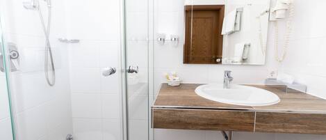 Ein Badezimmer mit einer gläsernen Duschkabine, einem Holztischchen inklusive Waschbecken und einem Spiegel darüber.