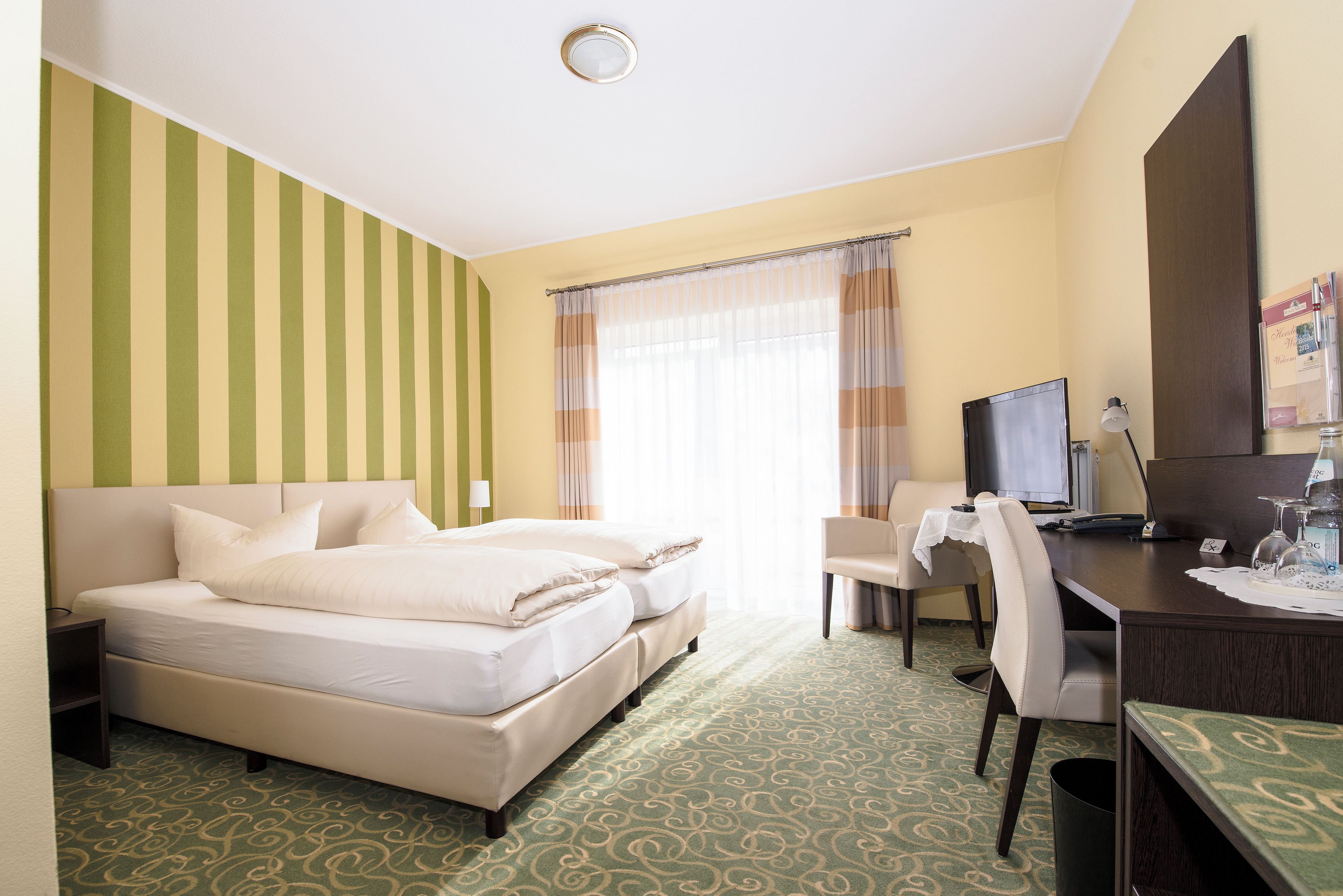 Una camera d'albergo con due letti, una scrivania, una sedia, una televisione e una finestra con tende.