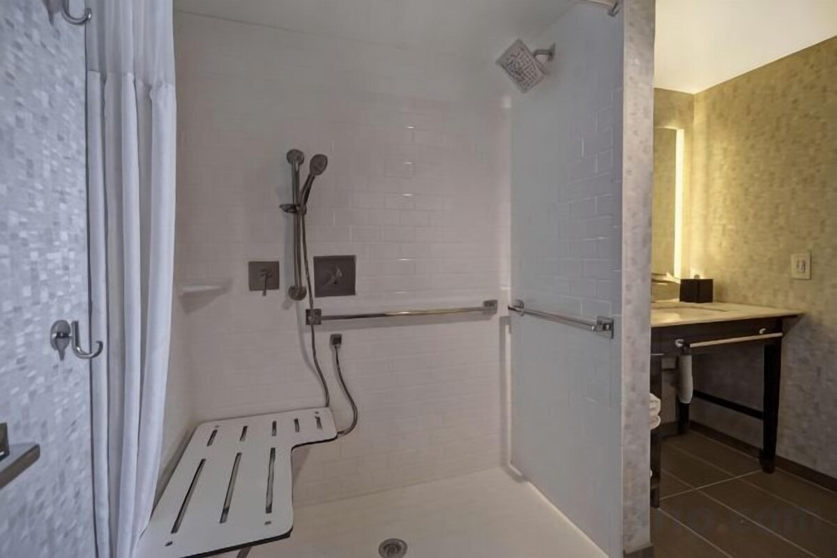 Une douche à l’italienne avec une barre d’appui, des toilettes et un lavabo équipé d’un porte-serviettes.