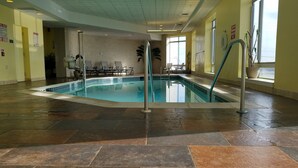 Una piscina interior con suelo de baldosas, una escalera de piscina y sillas alrededor.