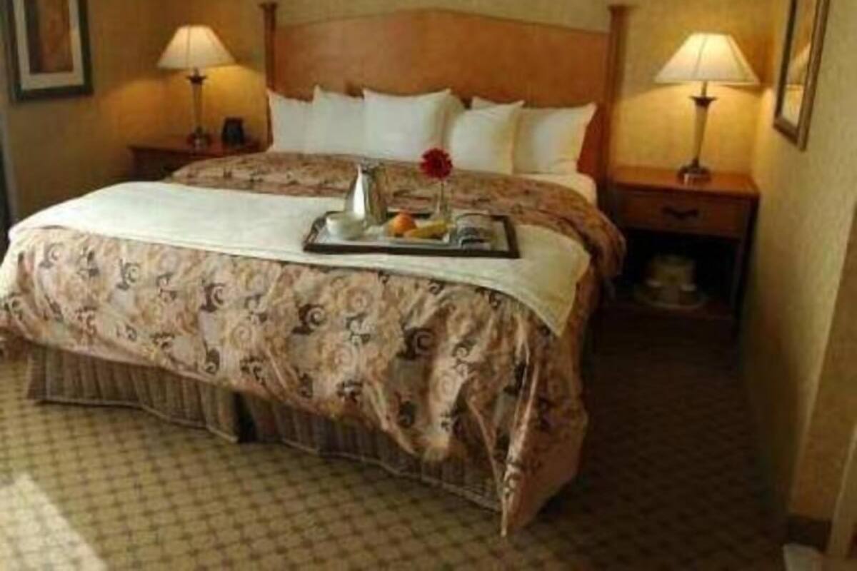 Habitación de hotel con cama, dos lámparas de noche, una bandeja con frutas y un jarrón, y una colcha estampada.