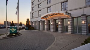 Entrada de un hotel con un camino curvo, un letrero de Homewood Suites y banderas.